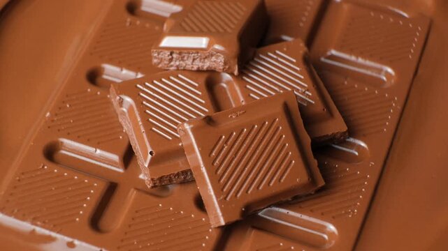 Milk chocolate bars and squares rotating in smooth melted chocolate pool