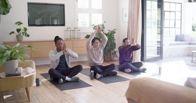 Three people following guided cue, bringing palms together, forming mudras on mats in living room