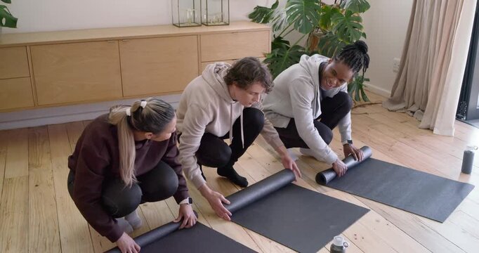 Diverse friends arriving, unrolling black mats in living room, coordinating to start workout