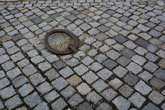 View of a weathered iron mooring ring embedded in traditional grey cobblestone pavement in Budapest, Hungary.
