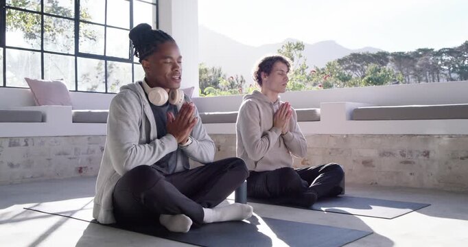 Diverse male friends sitting on mats in sunroom, following headphone cue, mirroring hand shifts