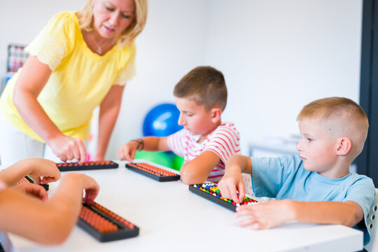 Group of children practicing mental arithmetic and counting with abacuses during a lesson with their teacher in a classroom.