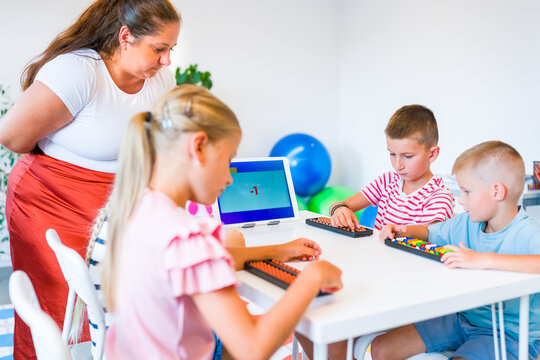 Teacher guides children practicing mental arithmetic and calculations with abacuses using a digital learning app during a classroom lesson.