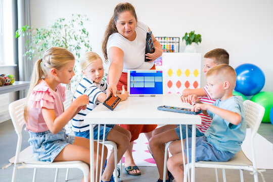 Teacher guides children practicing mental arithmetic and calculations with abacuses using a digital learning app during a classroom lesson.