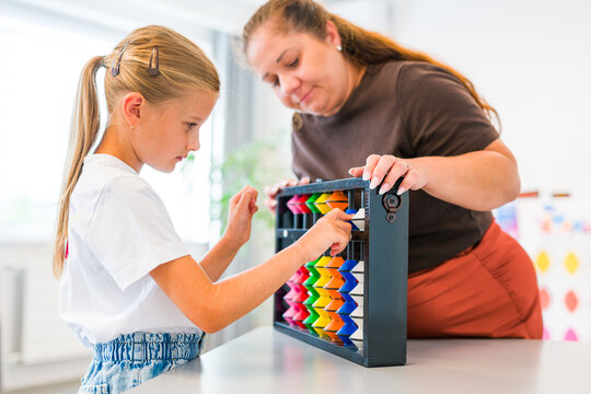 Teacher helps a young girl learn mental arithmetic and counting using a large colorful abacus during an educational lesson.