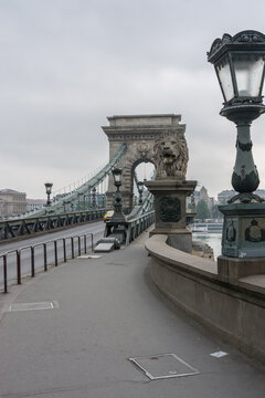 View of the stone lion statue guarding the entrance to the historic Szechenyi Chain Bridge with its ornate lamp posts and suspension structure in Budapest, Hungary.