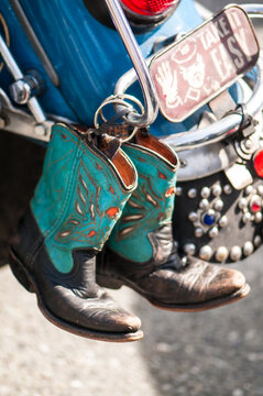 View of a pair of turquoise and black cowboy boots hanging from a motorcycle with a decorative license plate in Canada.