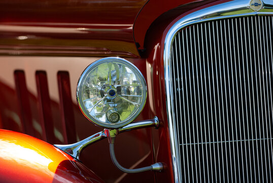 View of a vintage red car featuring a polished chrome grille and a round headlight in Langley, British Columbia, Canada.
