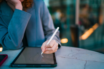 Close up of Caucasian female freelancer hand drawing vector balloon artwork with stylus pen on tablet screen, managing remote freelancing deliverables and digital nomad lifestyle projects © BullRun
