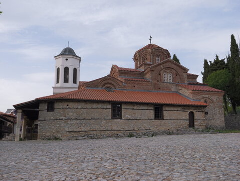 View of the Church of the Virgin Mary Peribleptos with its distinctive red-tiled roof, stone walls, and bell tower, set against a cloudy sky in Ohrid, Municipality of Ohrid, North Macedonia.