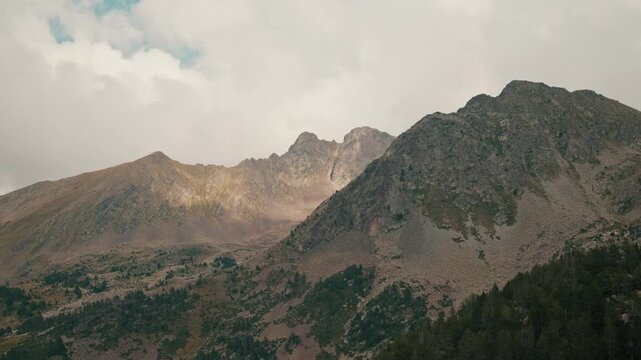 Majestic Pyrenean mountain peaks in Principality of Andorra, with Pinus uncinata pines, sunlight and cloudy sky backdrop. Scenic view of rocky mountain ranges at moody cloudy weather and sunlight play