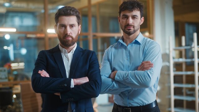 Two Caucasian authority business men crossed hands looking at camera serious in office. Calm businessmen male managers executives crossing arms posing together businesspeople unity corporate team