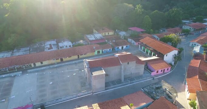 Aerial view of the village square and church in Cepe, surrounded by traditional houses with red tiled roofs under warm sunlight in Maracay, Aragua, Venezuela.