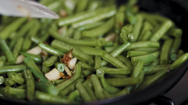 Cutting garlic over fresh green beans in a frying pan