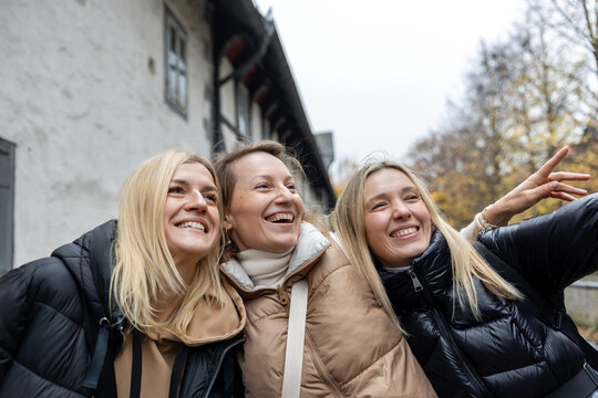 Cheerful friends laugh together on autumn city walk, sharing hugs and joyful travel moments. Candid group portrait captures friendship, reunion, happiness, leisure and weekend adventure outdoors