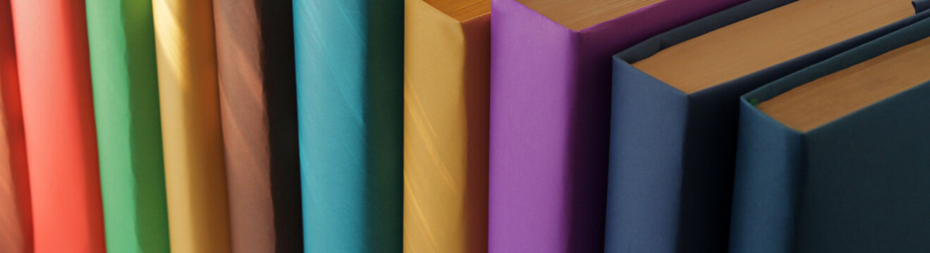 Books with colorful covers arranged in a row against multicolored paper backgrounds. A stack of books on a wooden table.