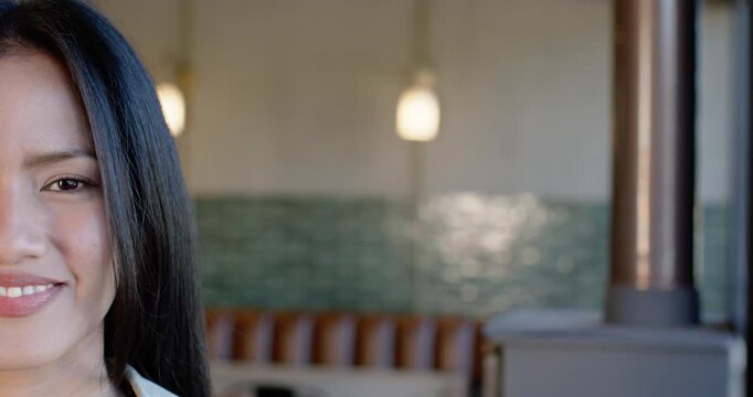 Mid-adult Asian woman opening eyes, causing wider grin at cafe booth lamps, collared top