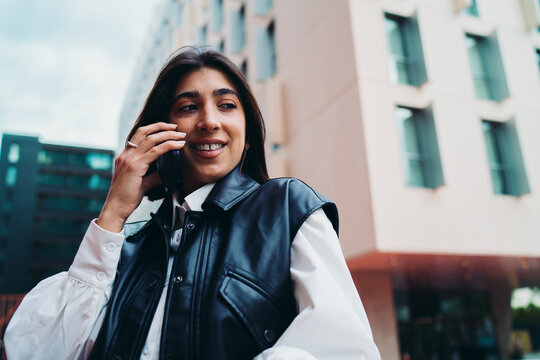 Spanish female talking mobile phone close up look away. Cheerful hispanic woman user communicating cellular network roaming application near abstract pastel architecture background surface.