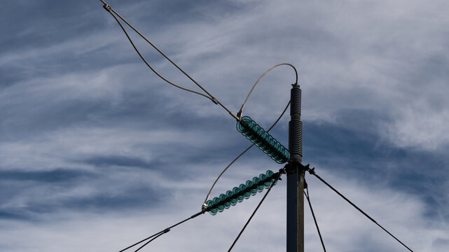 View of high voltage power lines with glass insulators on a metal pylon against a cloudy sky in Iceland.