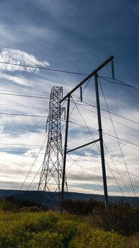View of high voltage power lines standing in a vast landscape under a dramatic blue sky with scattered clouds in Iceland.