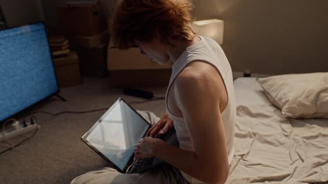 Caucasian young man typing on laptop, feeling exhausted from overworking, and lying back onto bed to rest. Footage fitting for remote work burnout, student fatigue, and wellness topics