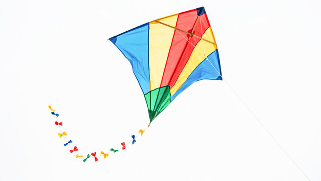 Vibrant multicolored kite flying high in the clear sky with a long trailing tail of colorful ribbons