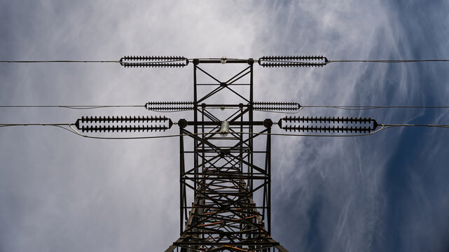 View of high voltage power lines on a metal pylon against a cloudy sky in Iceland.