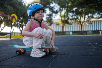 Cute Little Girl in Blue Helmet Sitting on Penny Board at Playground Outdoors © RealPeopleStudio