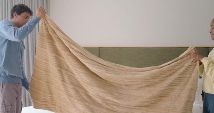 African American couple lifting beige blanket folding clothes at basket in bedroom while making bed