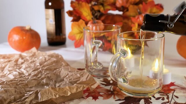 Person pouring beer into a glass mug on a table with an autumn tablecloth, capturing a Bavarian Oktoberfest celebration.
