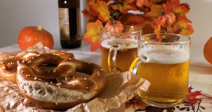 Person serving pretzels on a wooden board and beer mugs on an autumn tablecloth, highlighting national Bavarian culinary tradition