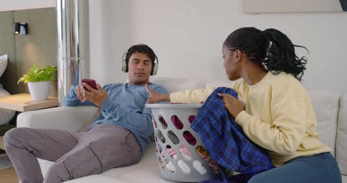 African American couple folding clothes on sofa from laundry basket after woman handing plaid shirt