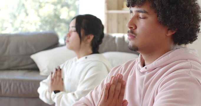 Couple pressing palms, sitting on mat at home, meditating and forming mudra for calm