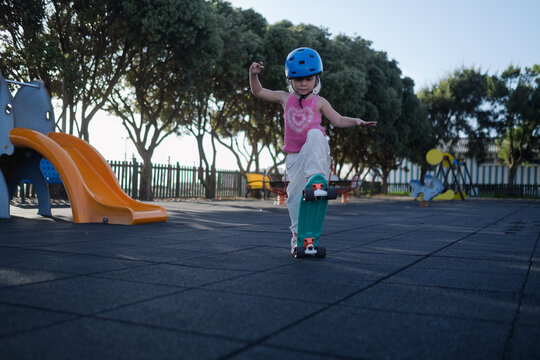 Little Girl in Blue Helmet Riding Penny Board and Balancing at Playground