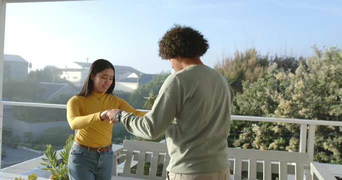 Couple holding hands, adjusting wristwatch while preparing twirl as man raising her arm on balcony