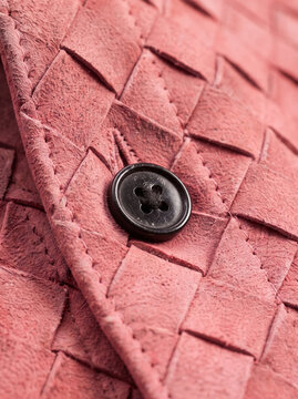 Close-up of pink woven leather with black button, textured fashion material detail