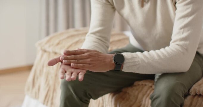 Camera pulling back, African American man rubbing hands self-soothing on bed in bedroom, smiling