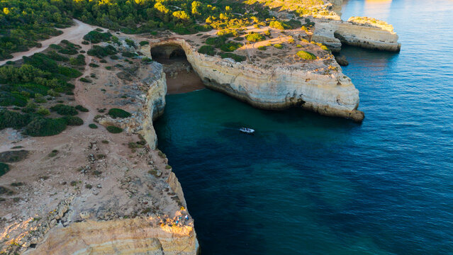 Picturesque coastal landscape of rugged limestone cliffs and clear turquoise water. Rocky cape over sea bay with stony shore under sunlight. Algarve, Portugal
