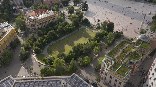 Aerial view of Skanderbeg Square featuring lush green park areas, historic architecture, the Et'hem Bey Mosque, and people walking across the expansive plaza in Tirane, Tirana County, Albania.
