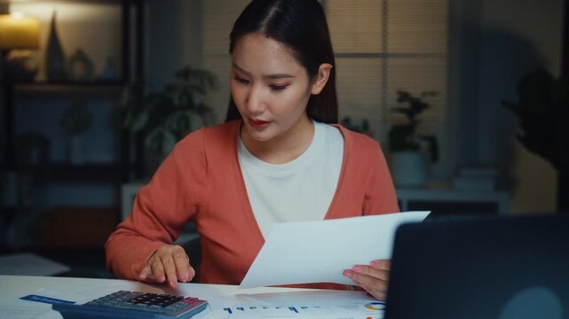 Young Asian woman calculates bills and household expenses with calculator and laptop at home at night. Personal finance budgeting, tax payment plan, debt control, savings mortgage management concept.