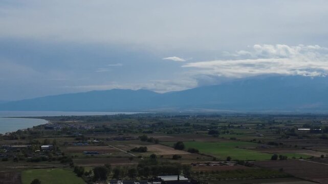 Aerial view of the majestic Mount Olympus partially covered by clouds above the agricultural plains of Paralia Katerinis, Pieria, Greece.