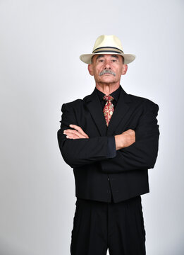 Selbstbewusster &auml;lterer Mann im schwarzen Anzug mit Hut und verschr&auml;nkten Armen vor neutralem Hintergrund. Charakterportr&auml;t, Business, Autorit&auml;t, Vintage-Stil und elegante Studiofotografie.