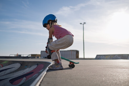 Determined Little Girl in Blue Helmet and Protective Pads Climbing Ramp with Skateboard at Skatepark