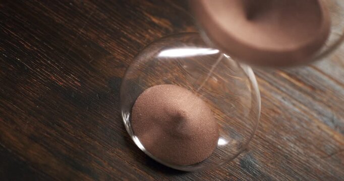 Hourglass with sand falling in super slow motion, evoking the passage of time, mortality, patience and the fleeting nature of life.