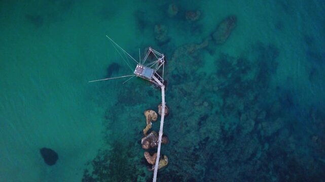 Aerial view of a traditional trabocco fishing structure on the Costa dei Trabocchi with turquoise sea and rocky coastline in Marina di San Vito, Abruzzo, Italy.