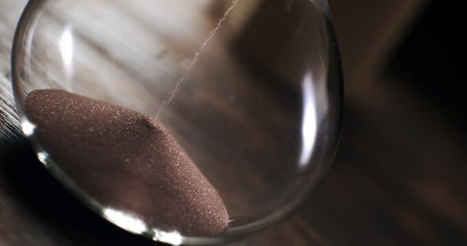 Cinematic slow motion close-up of an hourglass with sand falling through the narrow passage, symbolizing the passage of time, mortality, patience and the fleeting nature of life. 1000 fps.