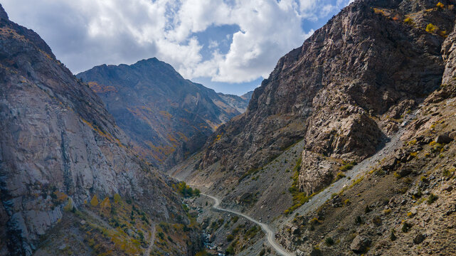 Aerial view of the rugged mountain landscape surrounding Deosai Top, featuring a winding dirt road through the valley with rocky slopes and autumn foliage in Skardu, Gilgit, Pakistan.
