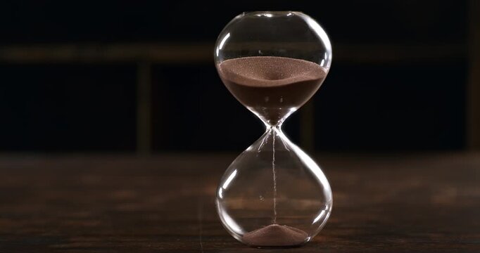Hourglass with sand falling in super slow motion, evoking the passage of time, mortality, patience and the fleeting nature of life.