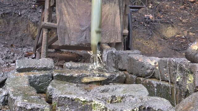 Traditional crude oil extraction using a pipe bailer at Teksas Wonocolo traditional oil field in Bojonegoro, East Java, Indonesia. Manual petroleum mining process from deep well with raw oil splash.