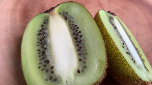 Camera zooming in slowly in real time toward a sliced green kiwi fruit displaying seeds and pulp on a round wooden cutting board. Soft natural daylight for food video concepts.